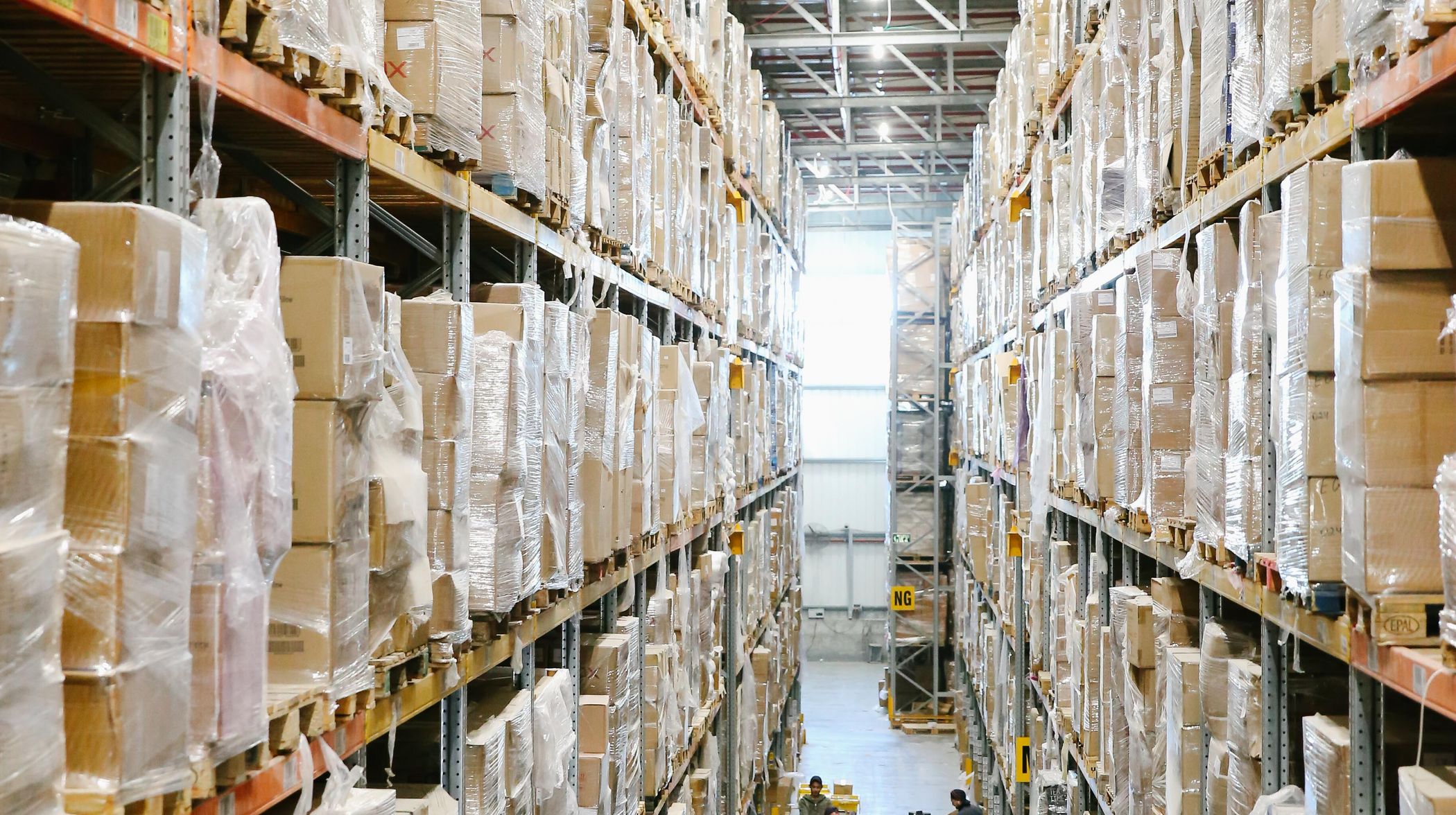 A tall warehouse aisle lined with shrink-wrapped pallets of boxes on steel racking.